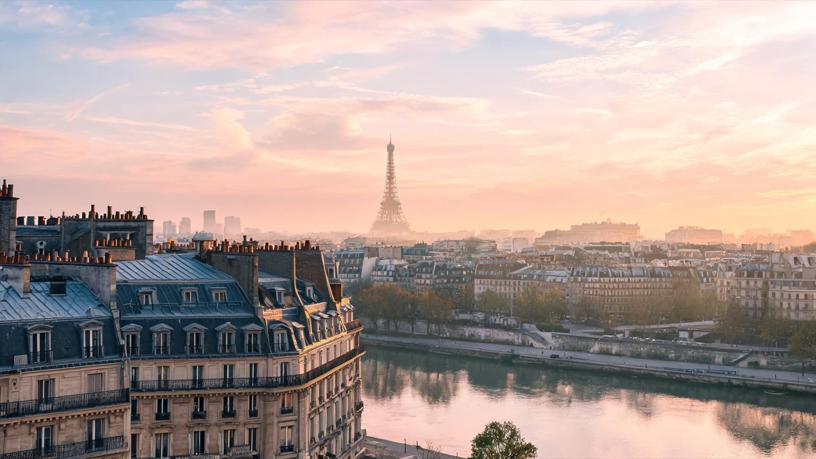 Paris rooftops and a quiet Seine embankment at sunrise with the Eiffel Tower softly in the distance