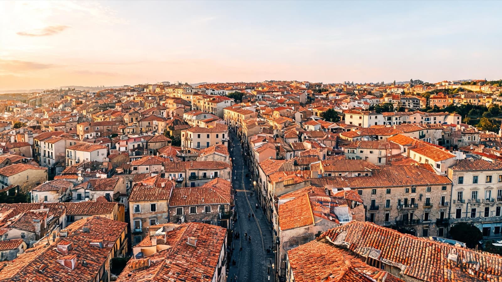 Aerial view of a historic city neighborhood with terracotta roofs and winding streets in late afternoon light