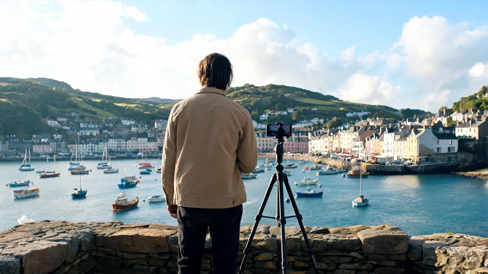 Traveler filming a scenic harbor with a phone on a small tripod, seen from behind